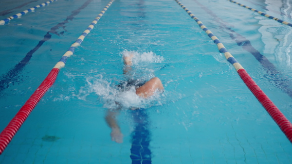 A mid adult man swimming in public indoors swimming pool.