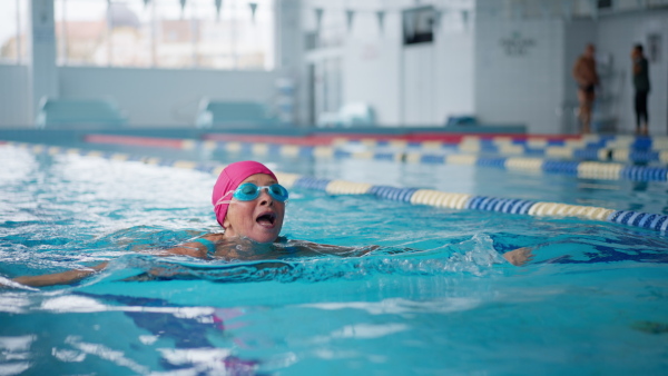 An active senior woman swimming in indoors swimming pool.