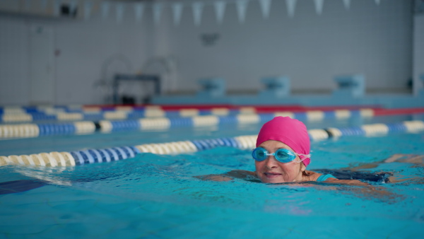 An active senior woman swimming in indoors swimming pool.