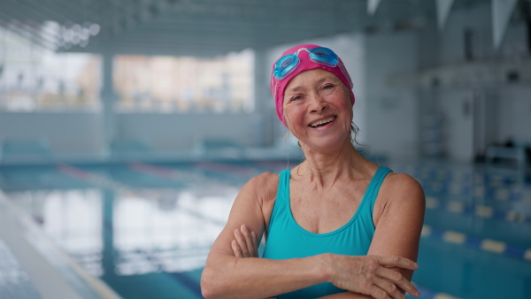 A happy senior woman after swim looking at camera in indoors swimming pool.