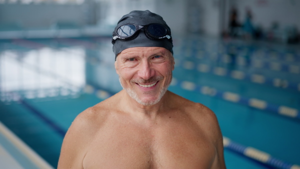 An active senior man looking at camera after swim in indoors swimming pool.