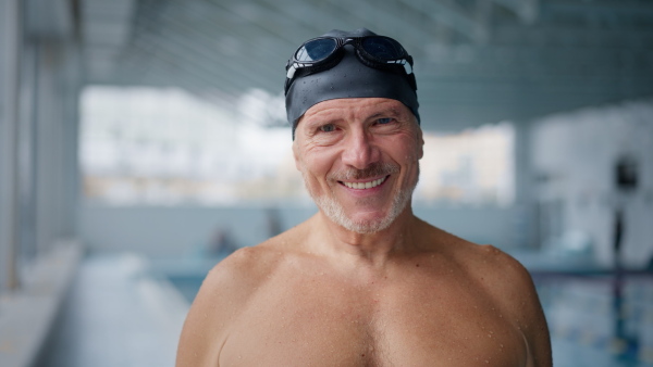 A senior man looking at camera after swim in indoors swimming pool.