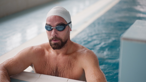 A mid adult man swimming in public indoors in swimming pool and looking at camera.