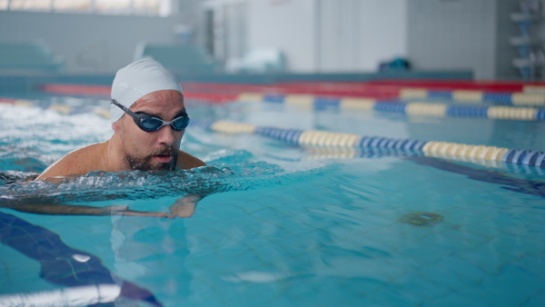 A mid adult man swimming in public indoors swimming pool.