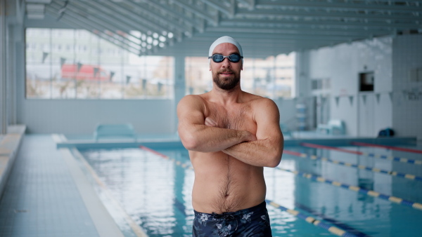 A mid adult man swimmer professional preparing to swim indoors in public swimming pool, looking at camera.