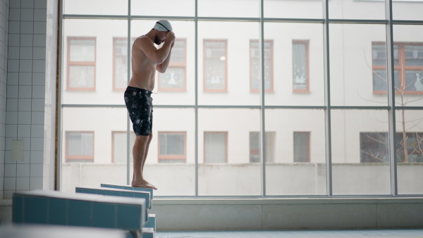 A mid adult man swimmer professional preparing to swim indoors in public swimming pool.