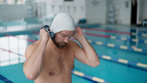 A mid adult man swimmer professional preparing to swim indoors in public swimming pool.