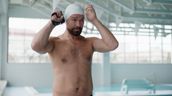 A mid adult man swimmer professional preparing for swimming indoors in public swimming pool.