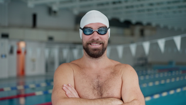 A mid adult man swimmer professional preparing to swim indoors in public swimming pool, looking at camera.