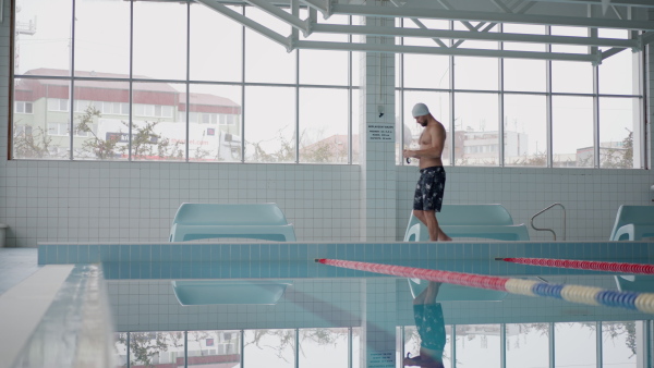 A mid adult man swimmer preparing for swim indoors in public swimming pool.