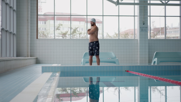 A mid adult man swimmer doing warming up exercise indoors in public swimming pool.