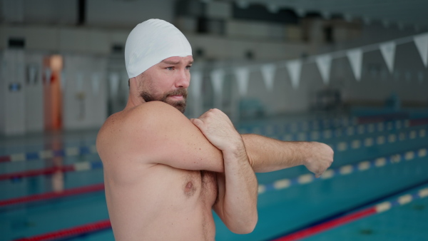 A mid adult man swimmer professional doing warming up exercise indoors in public swimming pool.