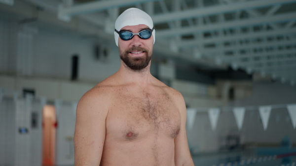 A mid adult man swimmer professional preparing to swim indoors in public swimming pool, looking at camera.