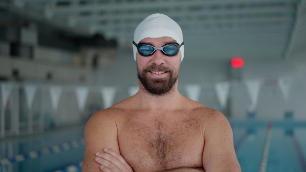 A mid adult man swimmer professional preparing to swim indoors in public swimming pool, looking at camera.