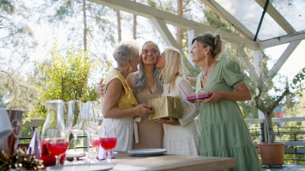 A happy senior woman getting presents from friends during birthday party outdoors on patio