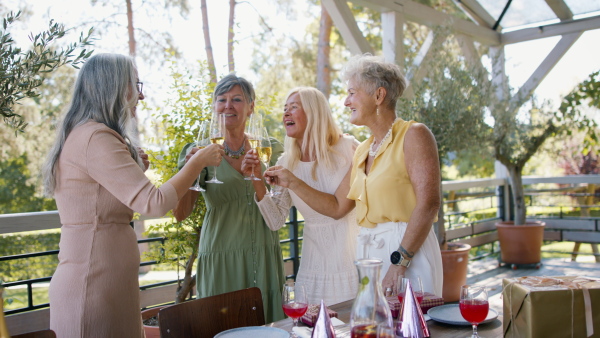 Happy senior women friends clinking glasses with champagne during celebration outdoors at terrace.