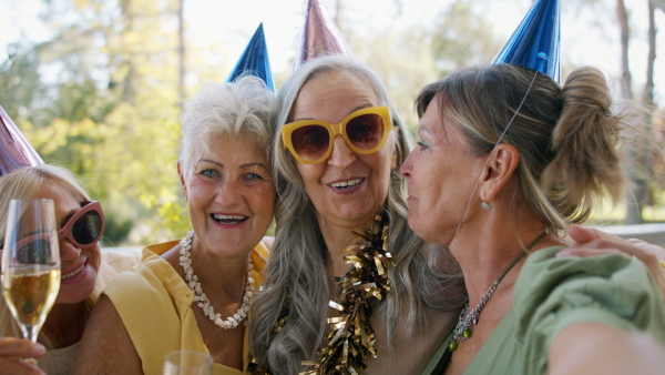 A close up of senior women with party hats celebrating birthday, singing and looking at camera