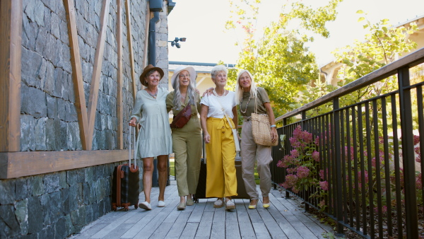 Happy senior women friends with suitcases arriving to a hotel for summer vacation and looking around excitingly.