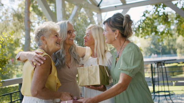 A happy senior woman getting presents from friends during celebration outdoors on patio