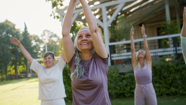 Senior women friends doing exercise outdoors in the park.