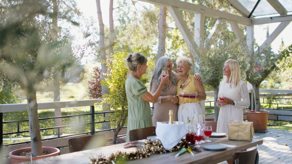 A happy senior woman getting presents and hugging with friends during celebration outdoors on patio