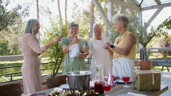 Senior women friends opening a champagne during celebration outdoors at terrace.