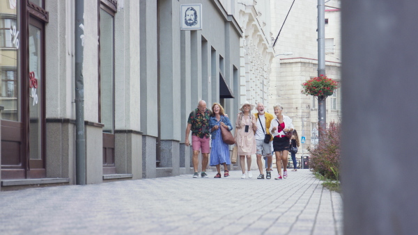 A group of happy senior friends tourists walking in city, laughing.