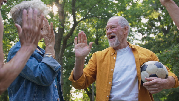 A group of happy senior friends having fun in city park, playing football.