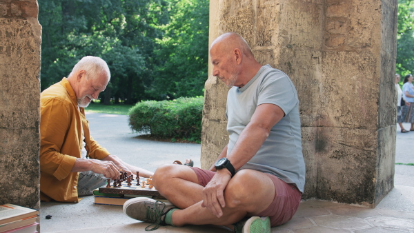 Happy senior men friends sitting outdoors in a city, playing chess.