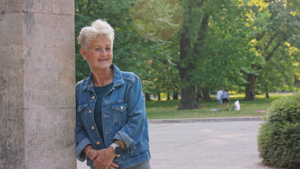 A happy senior woman in city park, looking at camera.