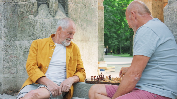 Happy senior men friends sitting outdoors in a city, playing chess.