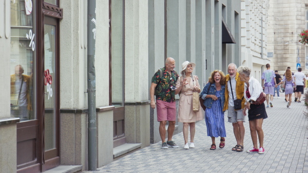 A group of happy senior friends tourists walking in city, laughing.