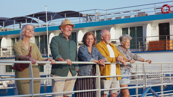 A group of happy senior friends tourists standing in city harbour, talking and looking to camera.