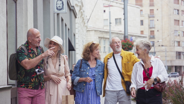 A group of happy senior friends tourists walking in city, laughing.