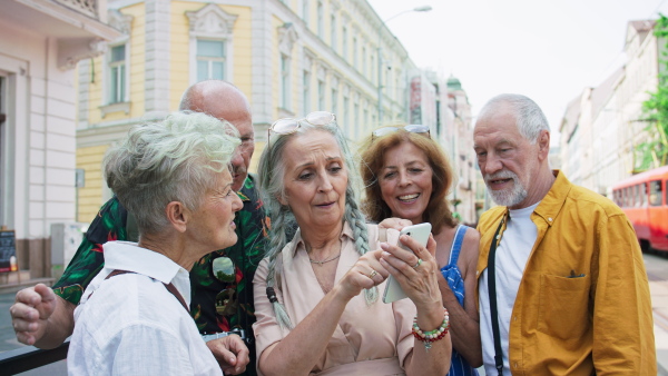 A group of happy senior friends tourists on a walk in city, using smartphone.