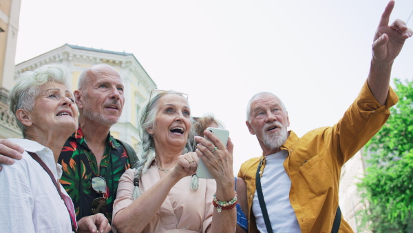 A group of happy senior friends tourists on a walk in city, using smartphone.