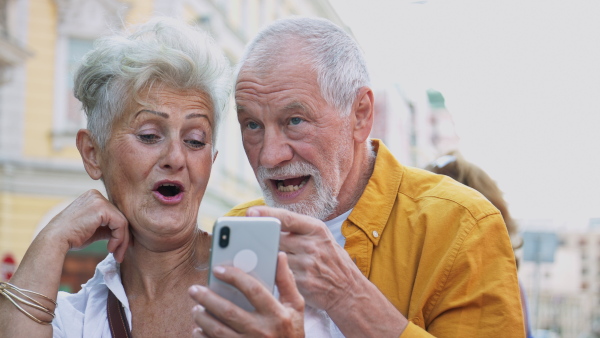 A happy senior couple tourists on a walk in city, using smartphone.