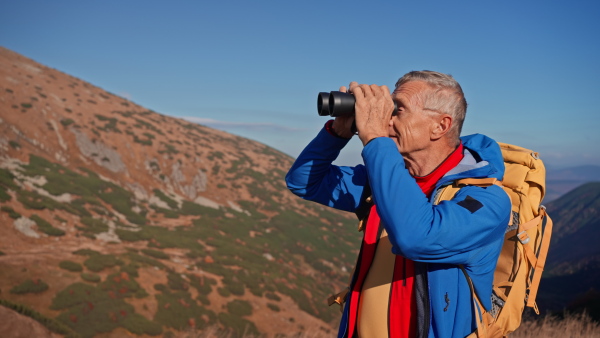 A senior man with binoculars looking at view when hiking in mountains.