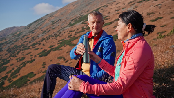 A senior couple hikers having break, sitting and drinking in mountains.