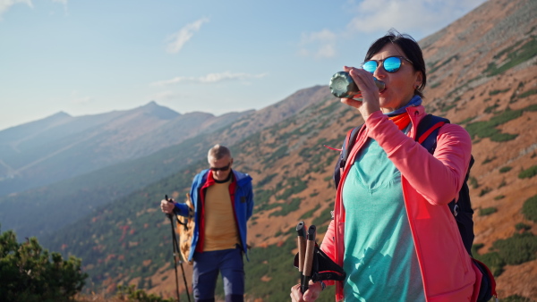 A senior couple hikers having break and drinking water in mountains.