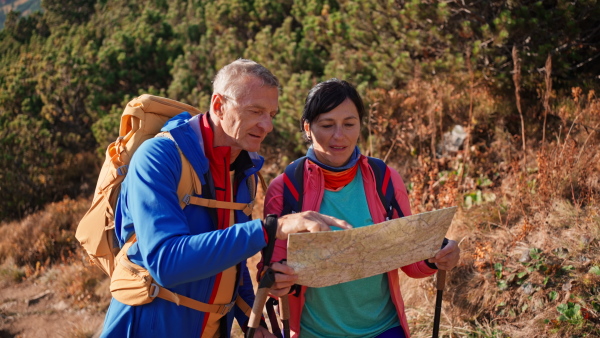 A happy senior couple hiking in mountains together, using map.