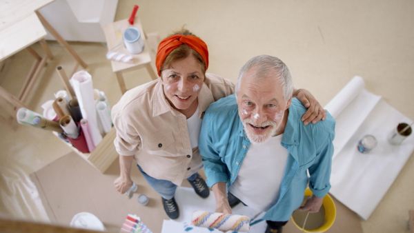 A top view of senior couple renovating their new flat, painting walls and looking at camera.