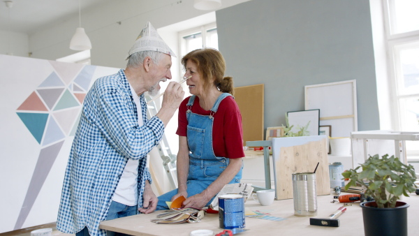 Beautiful senior couple renovating their new flat, having fun with paintbrush.