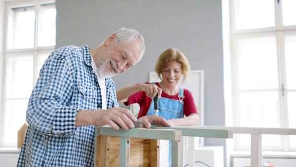 Beautiful senior couple renovating old wooden furniture.