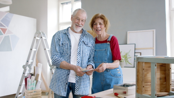 Beautiful senior couple renovating old wooden furniture, looking at camera.