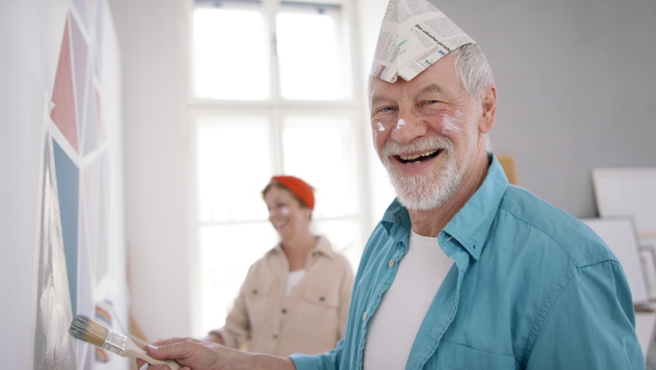 A side view of senior couple renovating their new flat, painting walls and looking at camera.