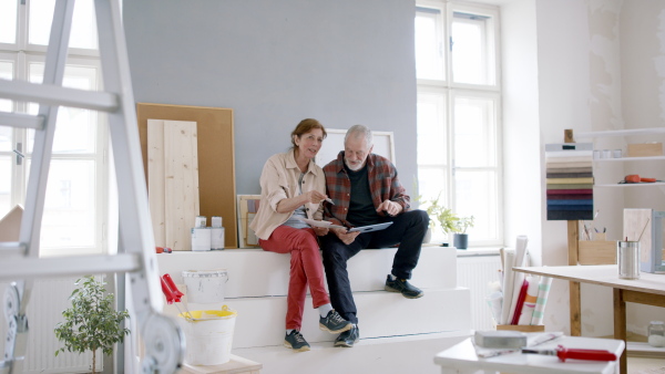 Beautiful senior couple planning the renovation of their new flat on tablet.