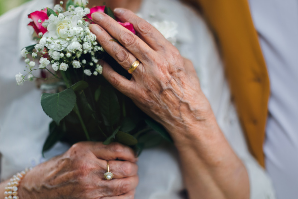 Close-up of senior hands with wedding bouquet and golden wedding rings during their marriage.