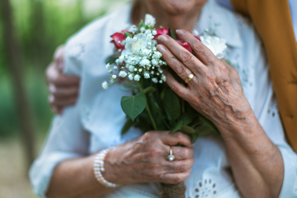 Close-up of senior hands with wedding bouquet and golden wedding rings during their marriage.