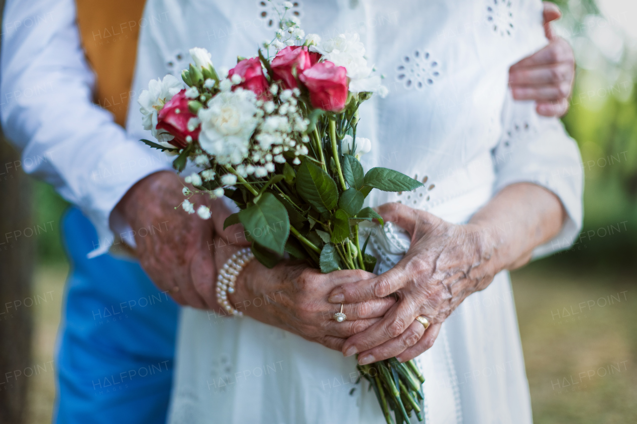 Close-up of seniors hands with wedding bouquet and golden wedding rings during their marriage.